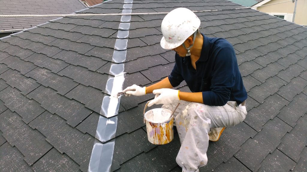 ストレート屋根の棟板金を刷毛で塗っている職人