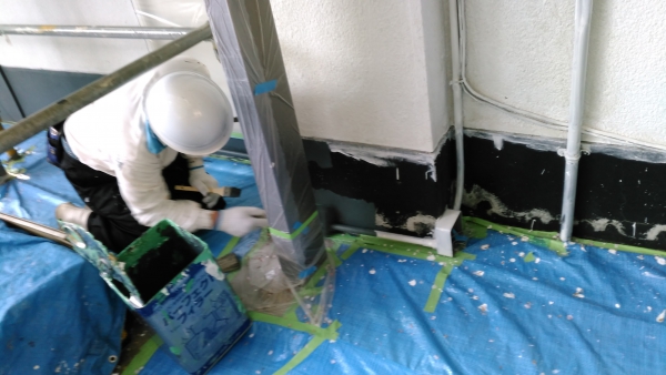 ブルーシートで養生された上で基礎を塗装する職人
